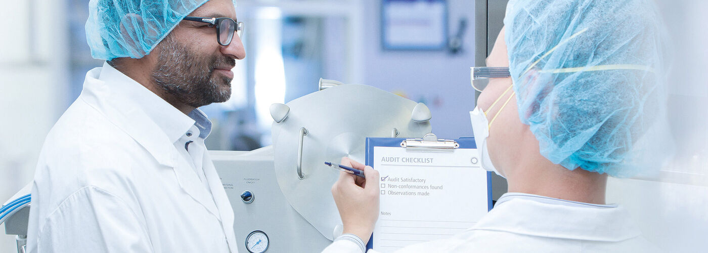 Deux employés de laboratoire en tenue de protection vérifient ensemble une liste de contrôle dans un environnement de production stérile.
