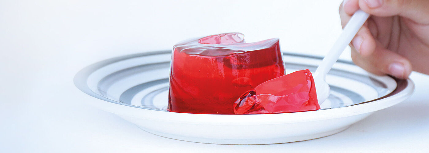 portion de dessert à la gélatine rouge sur une assiette à rayures, dont on retire un morceau à l'aide d'une cuillère blanche.