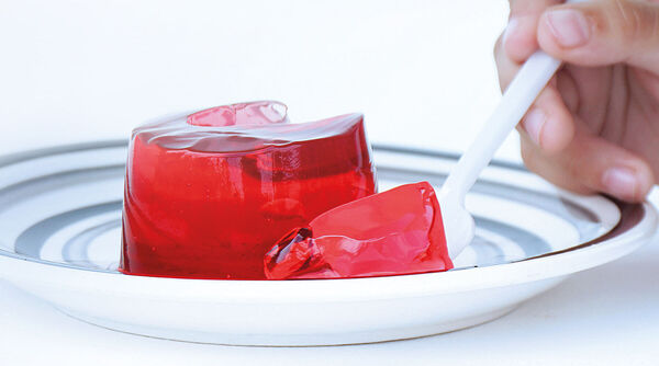 portion de dessert à la gélatine rouge sur une assiette à rayures, dont on retire un morceau à l'aide d'une cuillère blanche.