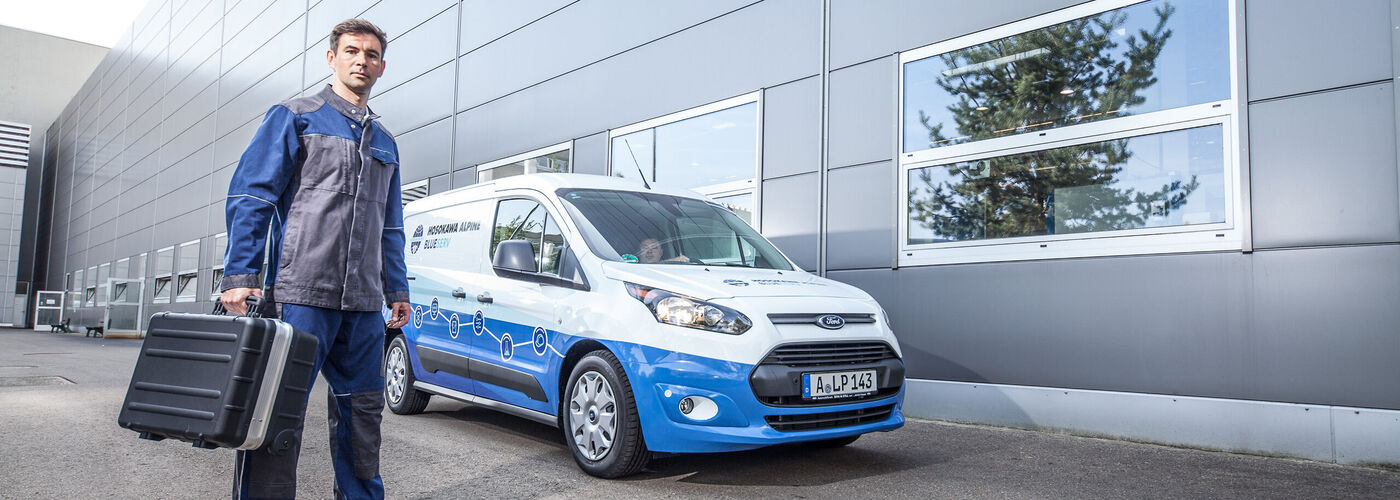 Un agent de service Blueserv avec une boîte à outils se tient devant une voiture Blueserv