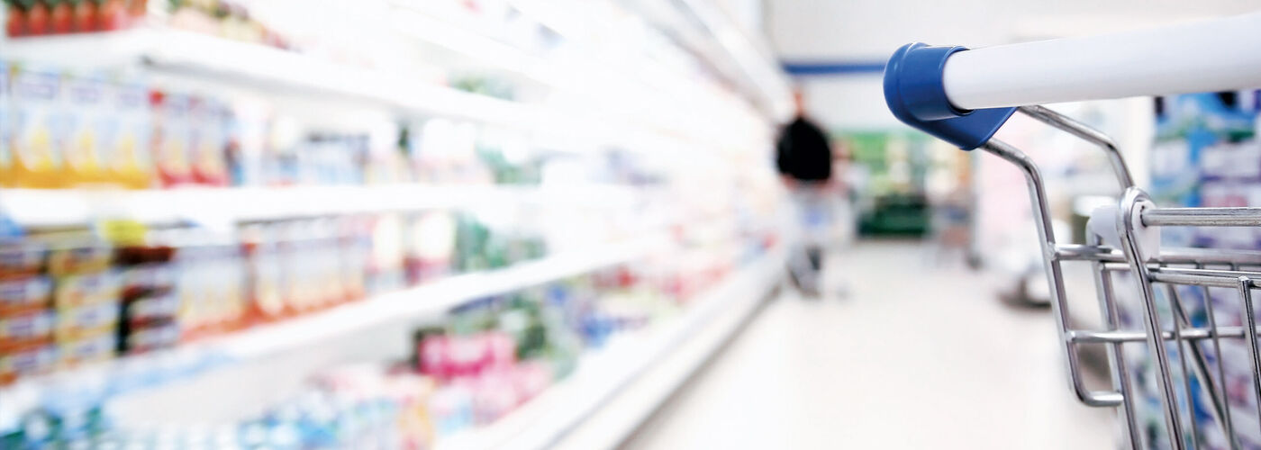 Supermarket shelf blurred with products, on the right is a shopping trolley