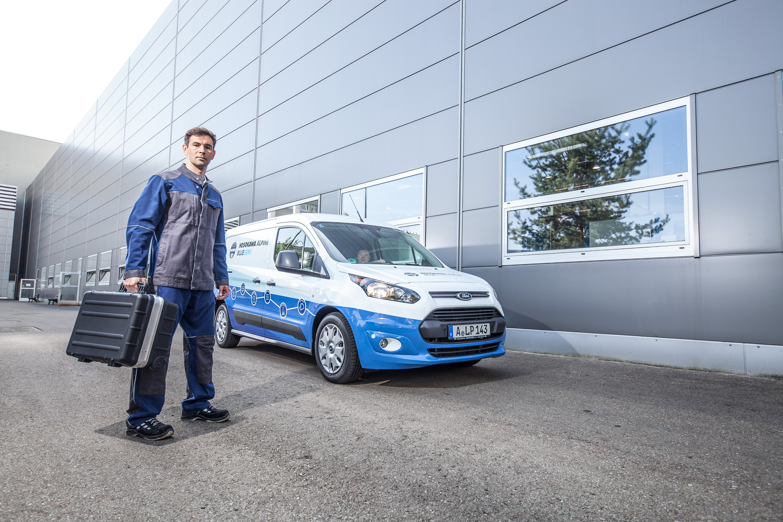 Un employé de Blueserv avec une boîte à outils devant une voiture Blueserv de marque