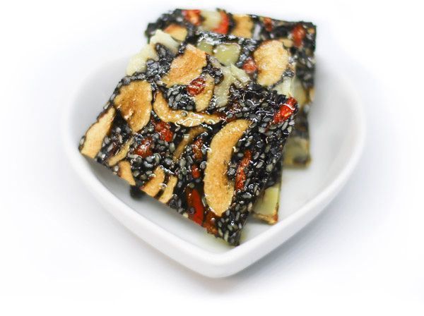  Fruits et graines enrobés de gélatine, en forme de biscuit carré. Trois pièces empilées sur une assiette ovale blanche